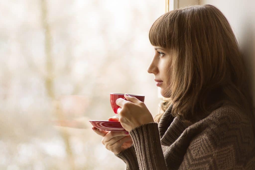 Beautiful girl drinking coffee or tea near the window